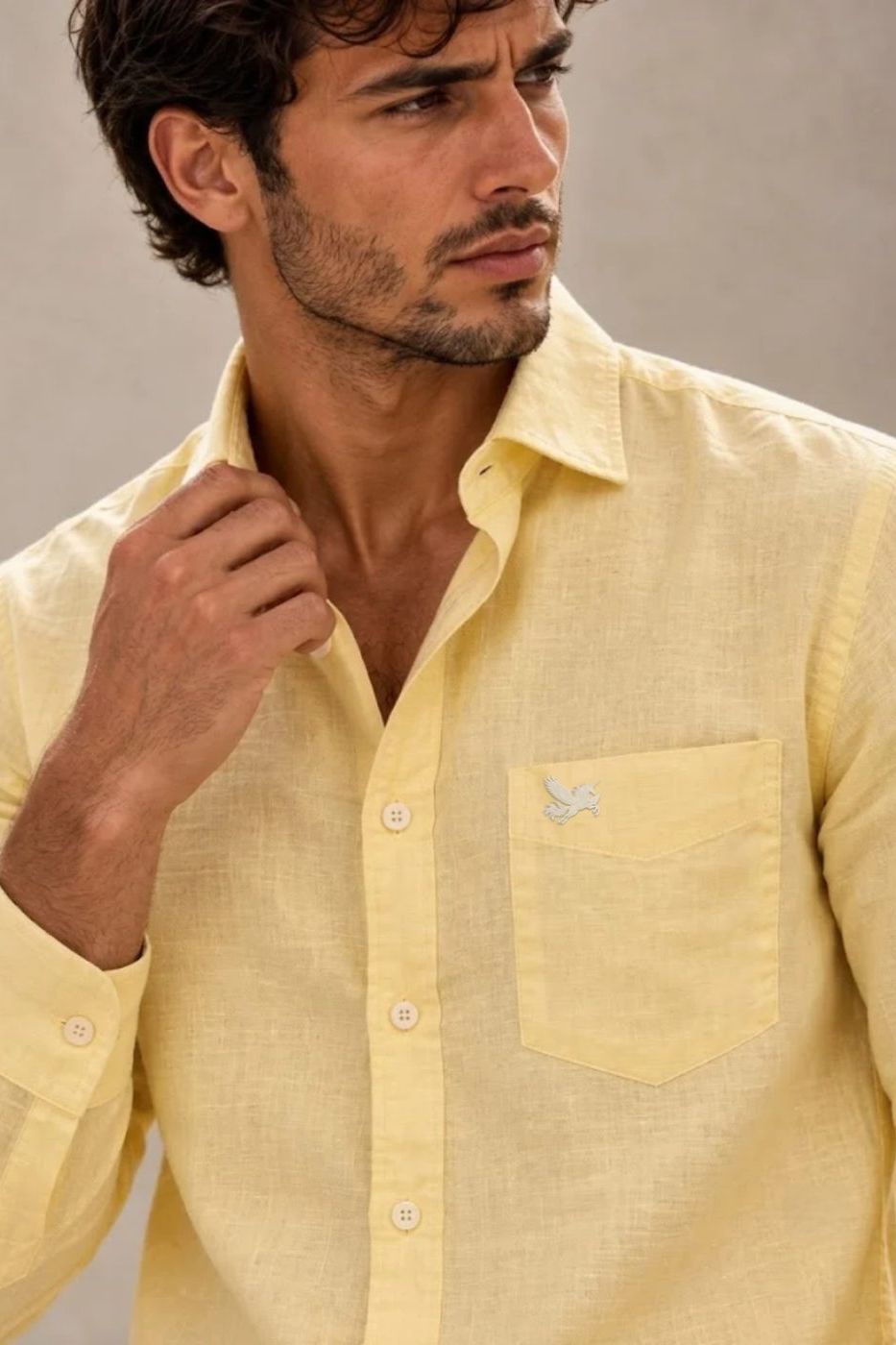 A man in a pale yellow linen shirt with a small unicorn embroidery